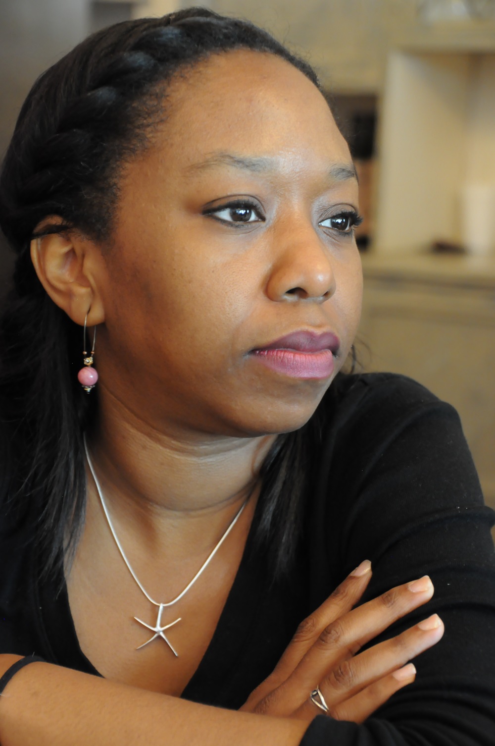 A photo of a woman with dark brown hair and a black shirt. She has her arms crossed and is looking out to the side.