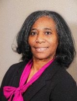 A photo of a smiling woman wearing a hot pink shirt and a black suit.