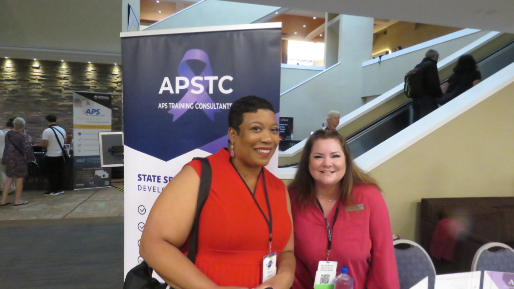 Two people smiling and standing in front of an exhibit booth.